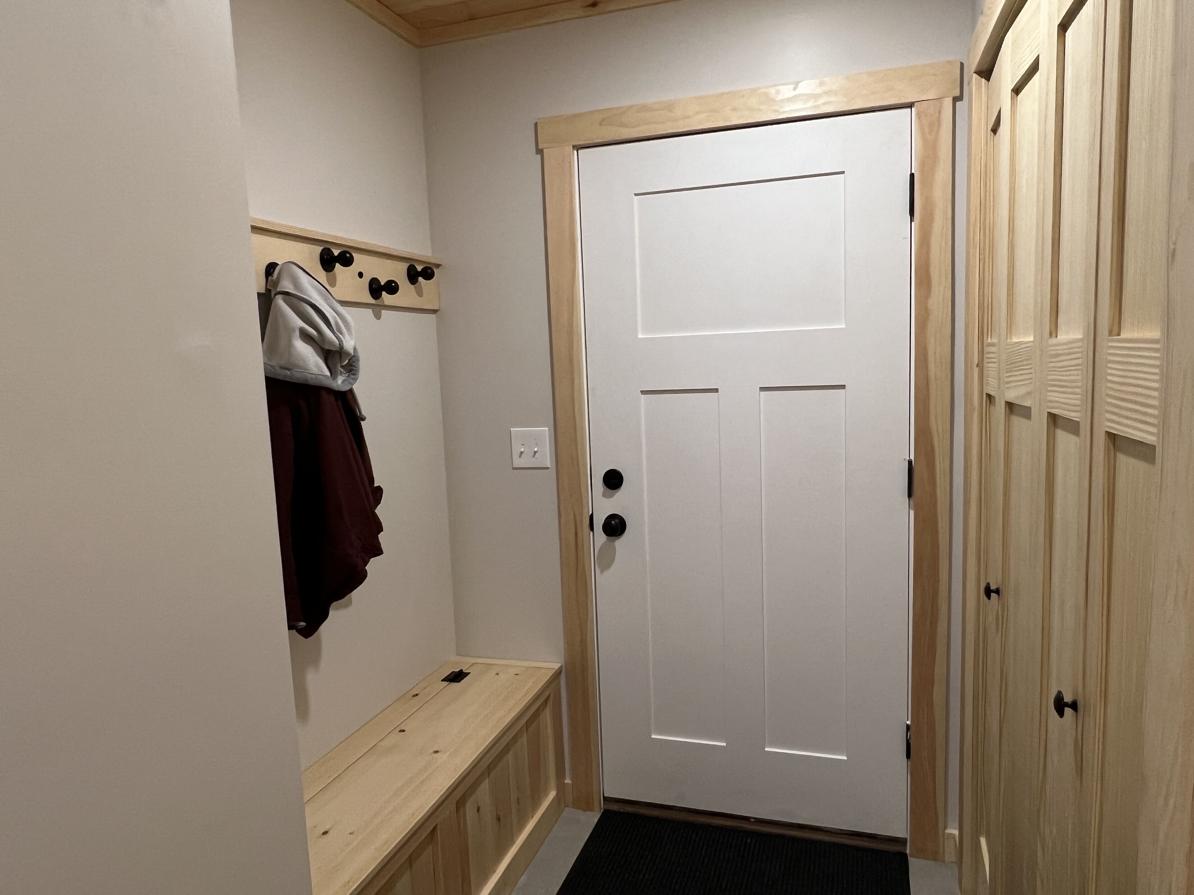 Un couloir avec une porte blanche, des armoires en bois et un banc.