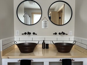 A bathroom with two round mirrors, a wooden vanity, and a sign above the mirrors. - Beautiful, brand new, cozy Maine cabin! (Dover-Foxcroft)