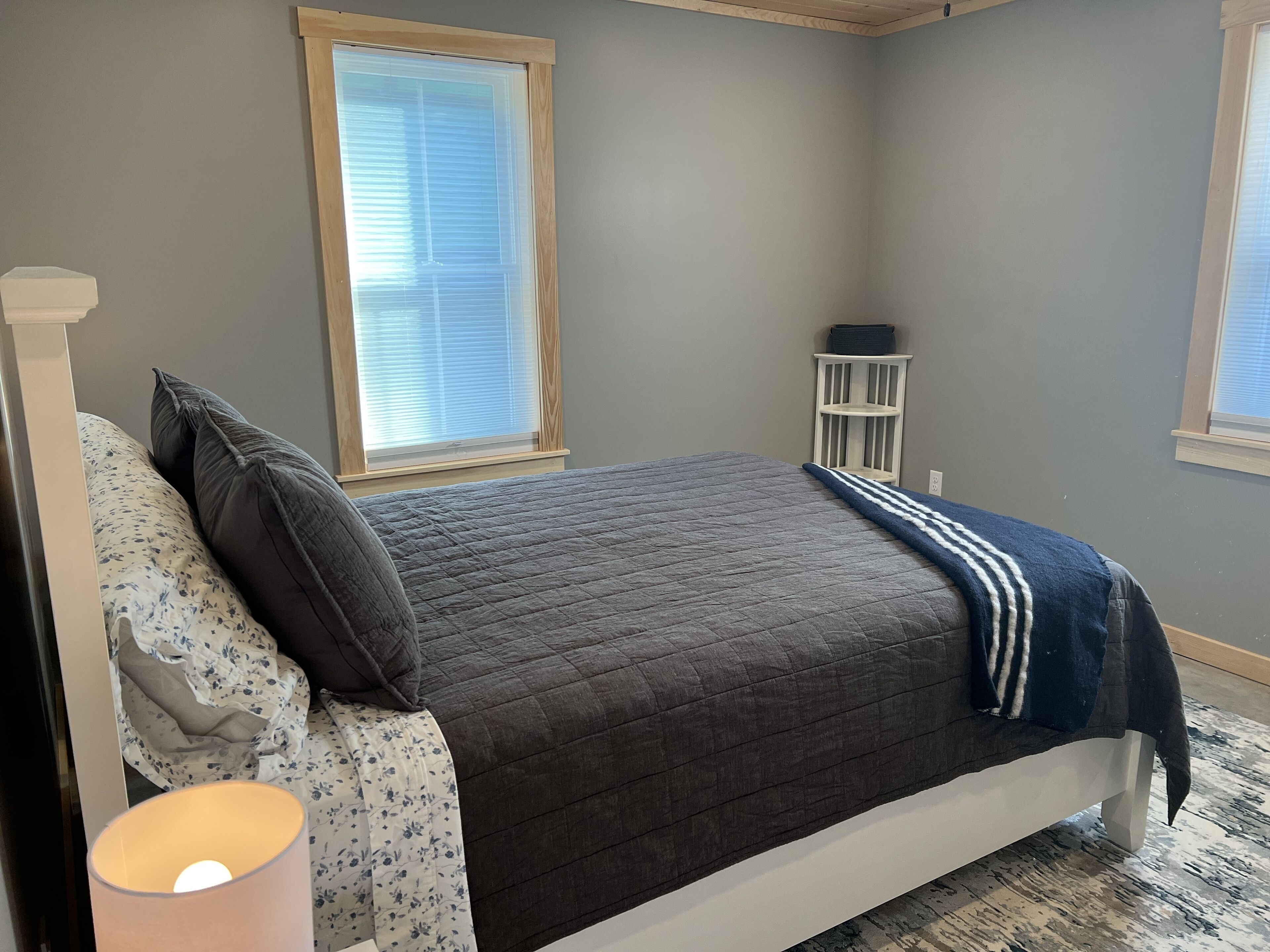 Un dormitorio con cama, mesita de noche, ventana y lámpara.
