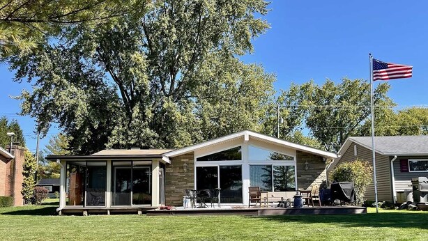 Une maison moderne dotée d’un patio couvert, de grandes fenêtres et d’un drapeau américain.