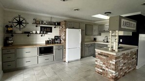 Une cuisine dotée d’un îlot central, de meubles blancs, d’un four à micro-ondes et d’un réfrigérateur.