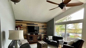 Un salon doté d’un ventilateur de plafond, d’un téléviseur à écran plat, d’un lambris en bois, d’un canapé, d’une table basse et d’une cheminée.