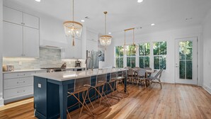 A modern kitchen with a central island, white cabinetry, and a large window offering a view of greenery. - Gather. Laugh. Repeat. Luxury in BMB – Bikes Included, Golf Cart Available (Santa Rosa Beach)