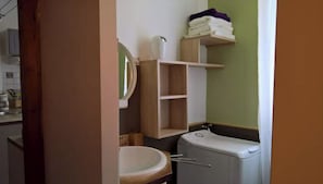 A bathroom with a toilet, sink, mirror, and shelves with folded towels.