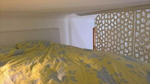 Ein Bett mit gelber Bettdecke mit Blumenmuster, einem Holzkopfschild und einem dekorativen Bildschirm mit geometrischem Muster.