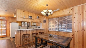 A wooden interior with a kitchen area, a dining table with four chairs, and a chandelier. - Hibernation Station I Near Snow Summit (Big Bear Lake)