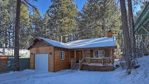 A log cabin with a porch and a garage, surrounded by a snowy landscape and tall pine trees. - Hibernation Station I Near Snow Summit (Big Bear Lake)