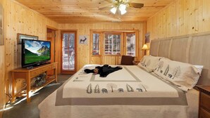 A wooden-paneled room with a bed, a television, and a ceiling fan. - Hibernation Station I Near Snow Summit (Big Bear Lake)