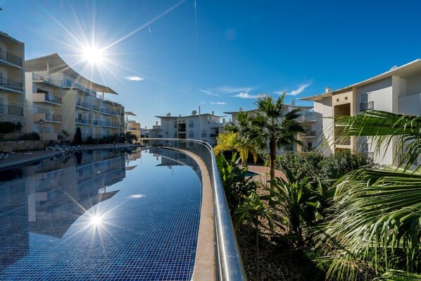 Una piscina de borde curvo, rodeada de palmeras y edificios modernos.