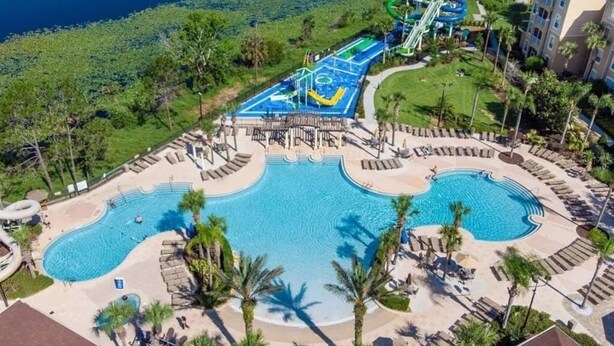 Un resort con una gran piscina central, un parque acuático y un césped bien cuidado.