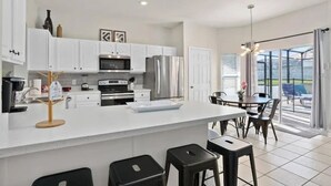 Una cocina moderna con armarios blancos, electrodomésticos de acero inoxidable y una isla central con taburetes.