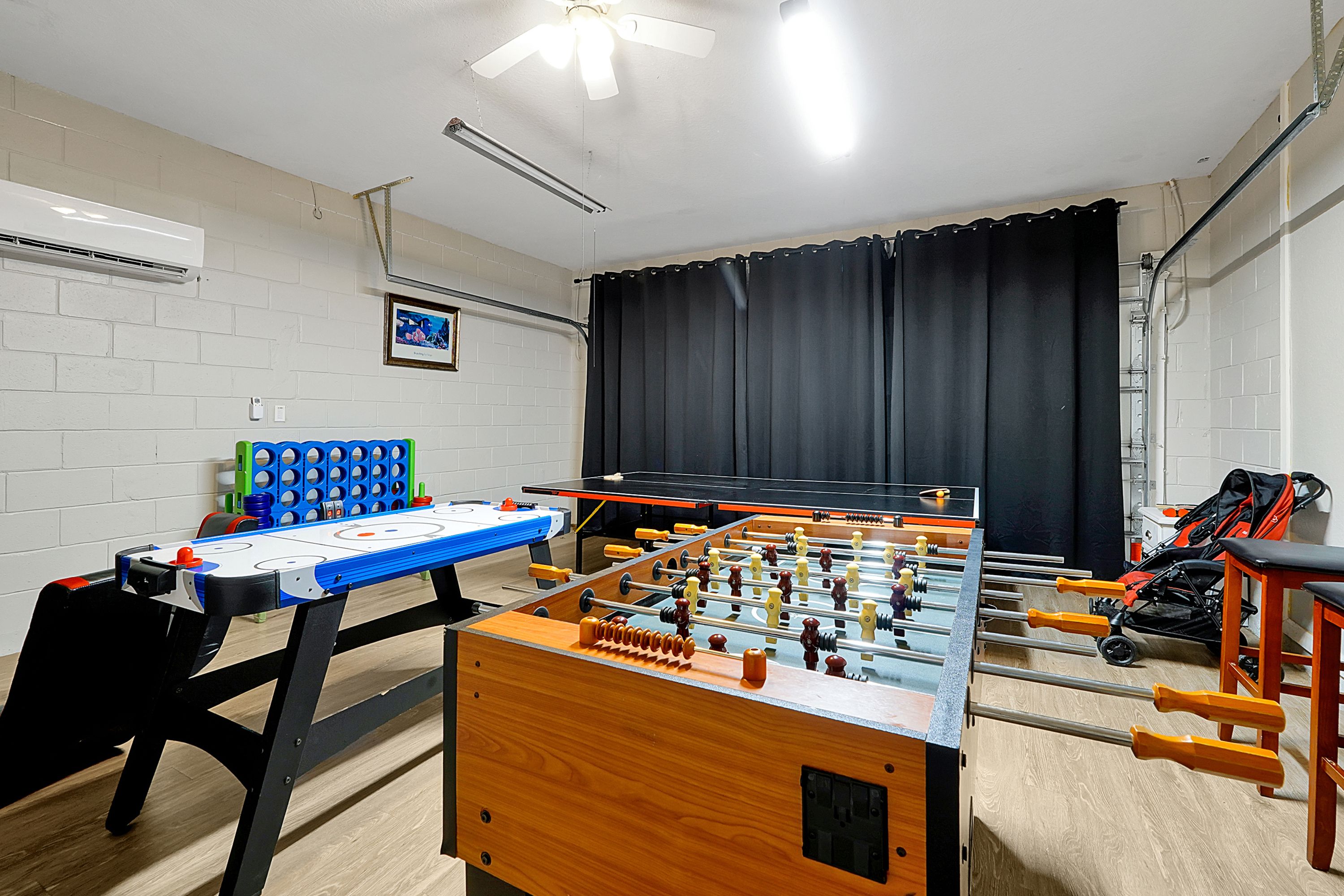 Una habitación con una mesa de fútbol de mesa, una mesa de tenis de mesa azul y otra mesa de fútbol de mesa con manijas naranjas.