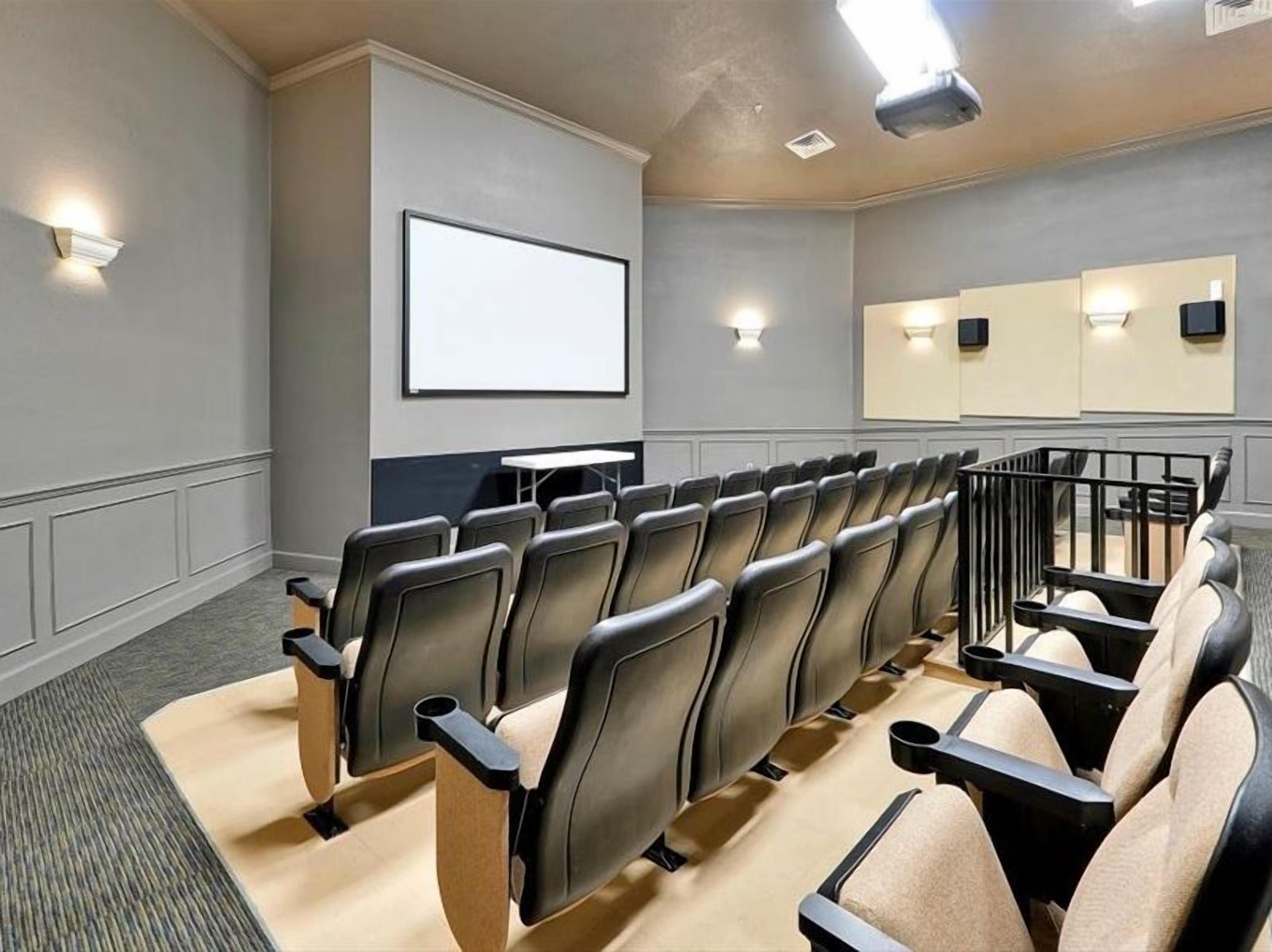 Un salón de conferencias con filas de sillas, una pantalla de proyección e iluminación empotrada en las paredes.