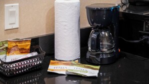 A hotel room counter with a coffee maker, a roll of toilet paper, and a basket containing a packet of tissues and a small item with 'ITALIA' branding.