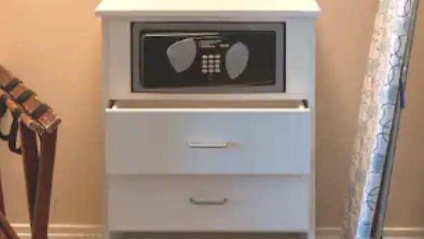 A white bedside table with a radio, a drawer, and a hanging coat rack.
