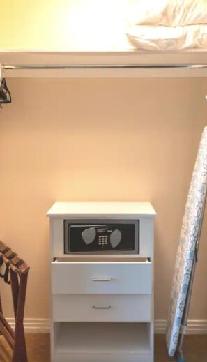 A white bedside table with a radio, a drawer, and a hanging coat rack.