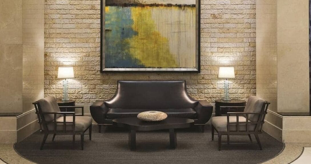 A lobby with a stone wall, a large abstract painting, a leather sofa, two armchairs, and two side tables with lamps.