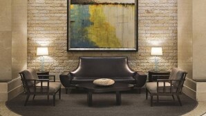 A lobby with a stone wall, a large abstract painting, a leather sofa, two armchairs, and two side tables with lamps.