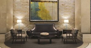 A lobby with a stone wall, a large abstract painting, a leather sofa, two armchairs, and two side tables with lamps. - MGM Signature Tower 2 | 8th Floor 2-Suite | Strip View Balcony | No Resort Fee (LAS VEGAS)