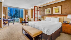 Ein Hotelzimmer mit einem großen Bett, einem Schreibtisch, einem Sessel, einem kleinen Tisch und einem Balkon mit Blick auf die Stadt.