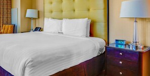 A hotel room with a large bed, a bedside table with a lamp, a clock, and a nightstand with drawers.