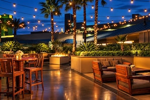 An outdoor seating area with wooden furniture, a fire feature, and string lights. - MGM Signature Tower 2 | 8th Floor 2-Suite | Strip View Balcony | No Resort Fee (LAS VEGAS)