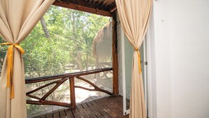 A wooden deck with a thatched roof, beige curtains tied with yellow ribbons, and a view of lush greenery outside. - Hotel Ak'Na Holbox (Isla Holbox)
