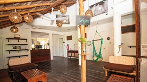 A spacious living area with dark wooden flooring, a central wooden pole with a 'Welcome' sign, and a green hammock hanging from it. - Hotel Ak'Na Holbox (Isla Holbox)