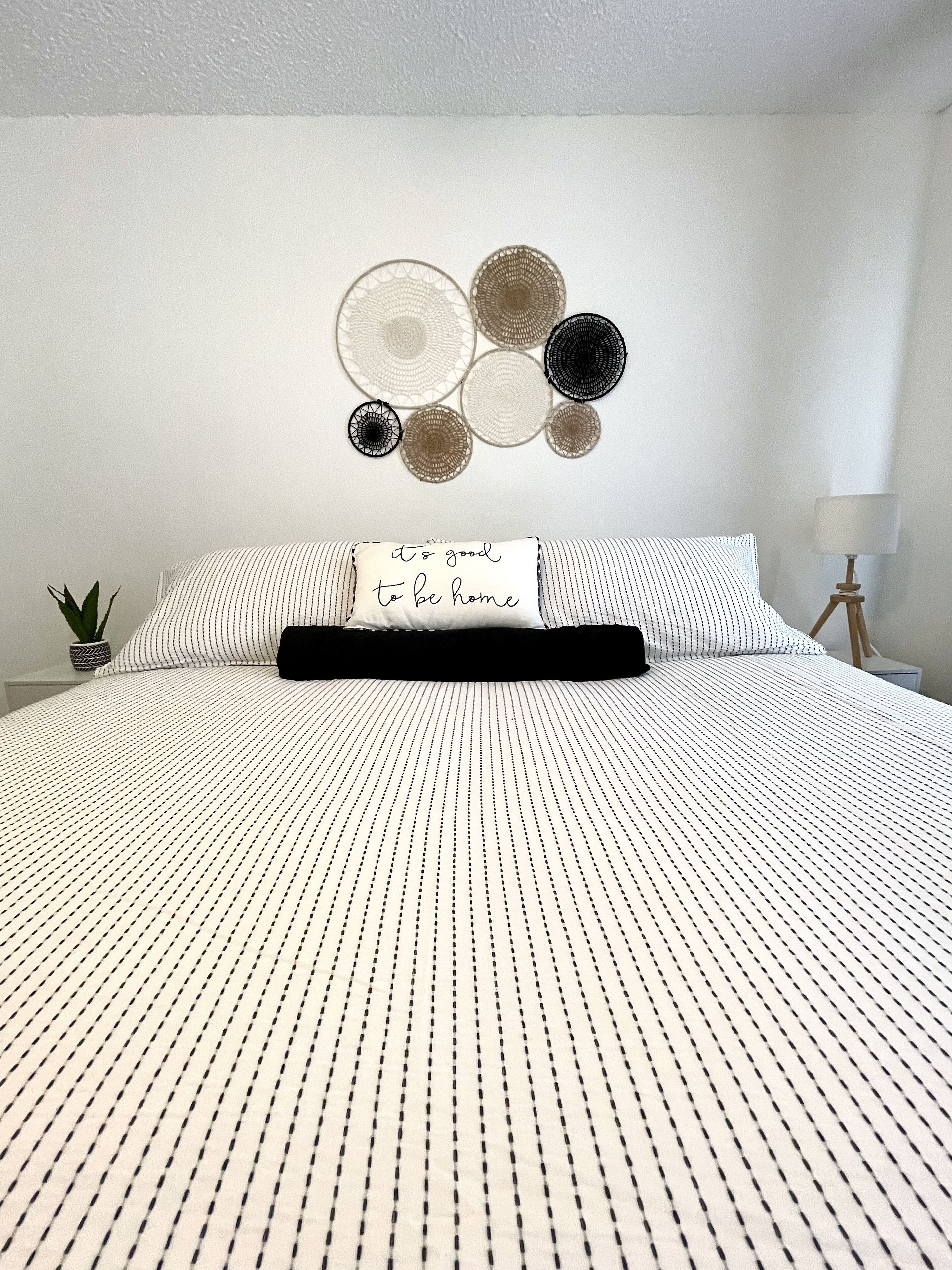 Een net opgemaakt bed met een gestreept dekbedovertrek, een kussen met een bemoedigende quote, en een muur met ronde decoraties.