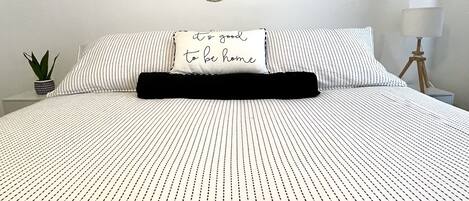 Een net opgemaakt bed met een gestreept dekbedovertrek, een kussen met een bemoedigende quote, en een muur met ronde decoraties.