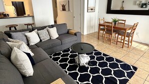 A modern living room with a sectional sofa, a round coffee table, and a dining area with a wooden table and chairs. - Inner City TownHome (Fort Worth)
