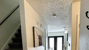 A staircase leading to a living area with a patterned rug, a dining table, and a door at the end. - Inner City TownHome (Fort Worth)