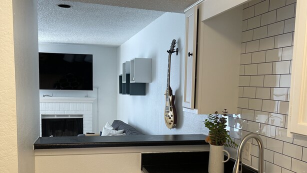 A compact kitchen with a black countertop, white cabinets, a stainless steel sink, a built-in microwave, and a wall-mounted TV. - Inner City TownHome (Fort Worth)