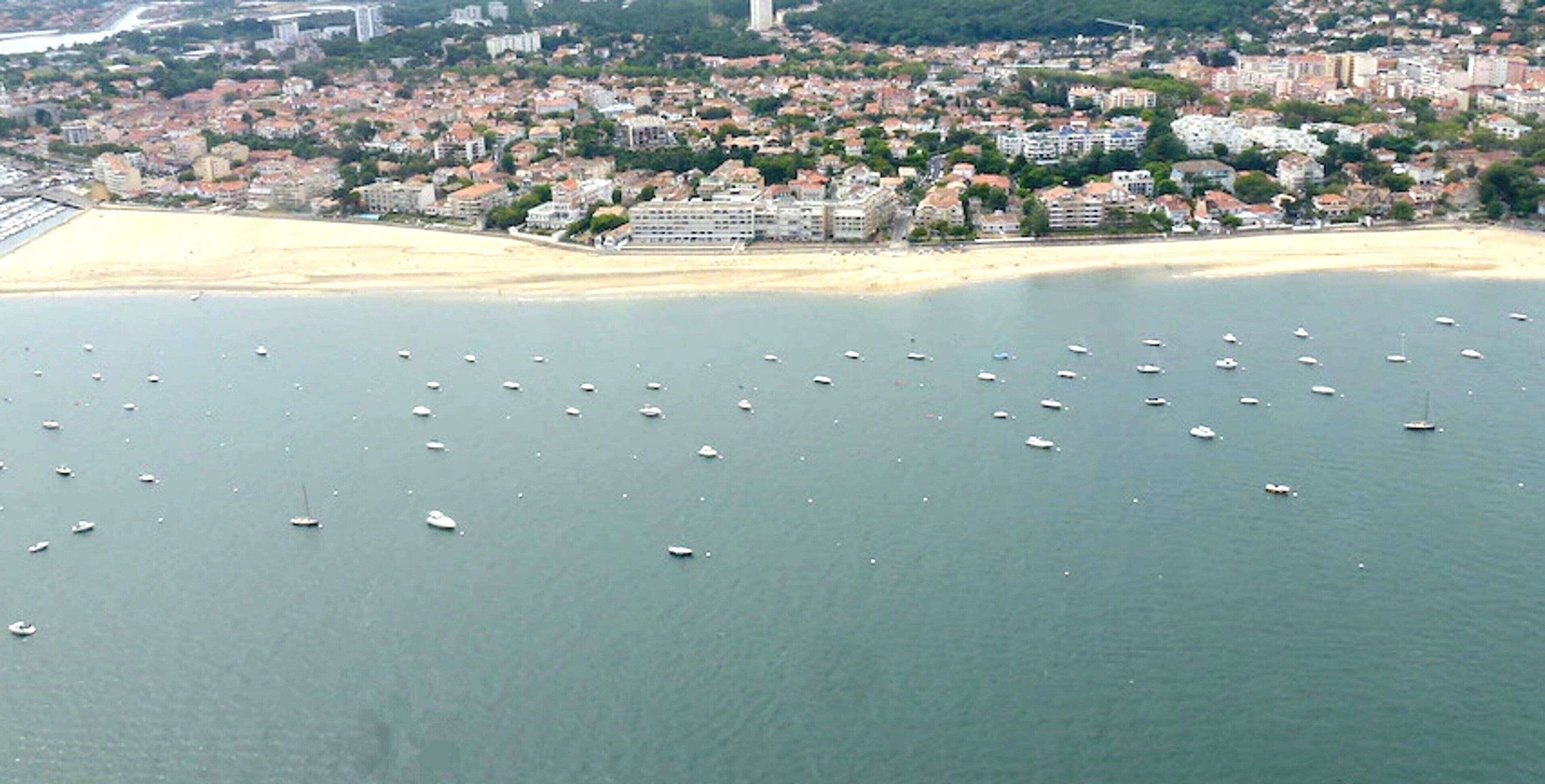 Vue aérienne d’une ville côtière avec une plage et de nombreux bateaux sur l’eau.