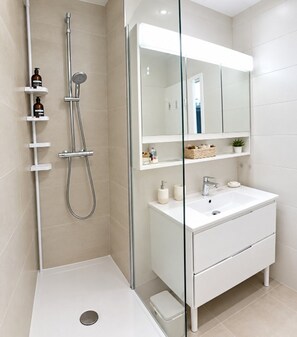 Une salle de bain moderne avec une douche à parois de verre, un lavabo blanc et une coiffeuse avec un grand miroir.