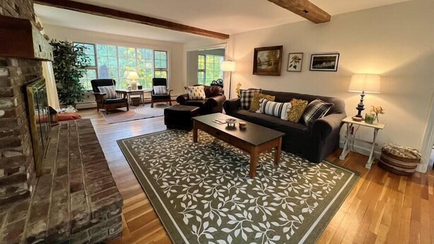 A spacious living room with a fireplace, wooden flooring, a large window, and a cozy seating area.
