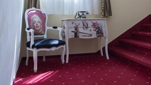 A room with a red carpet, a white chair with a cushion, a small table with a lamp, and a staircase. - Barock Jimbolia (Jimbolia)