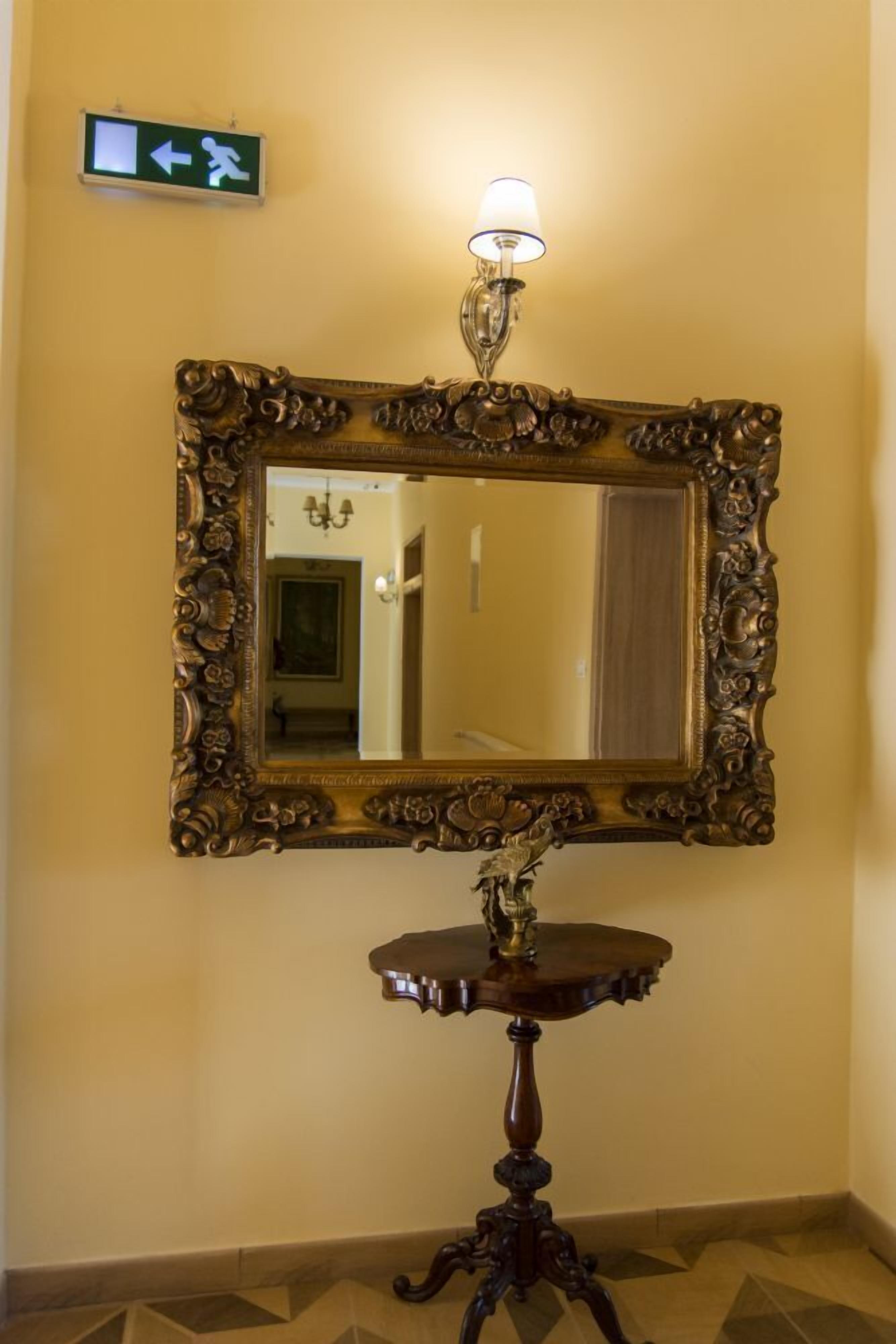 A mirror with an ornate frame, a small table with a lamp, and an exit sign on the wall.