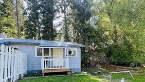 A small, single-story house with a porch and a fenced yard, surrounded by trees. - Mountain Bungalow (Martin City)