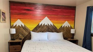 A hotel room with a bed, two bedside tables, and a wall mural. - Mountain Bungalow (Martin City)