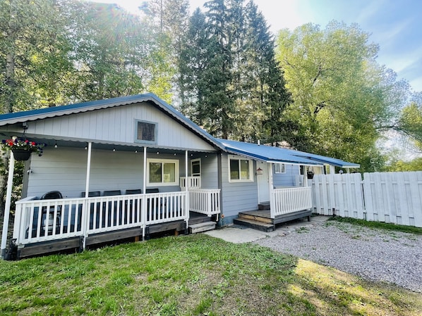 A single-story house with a porch, a covered outdoor seating area, and a white picket fence. - Blue Bird Bungalow (Martin City)