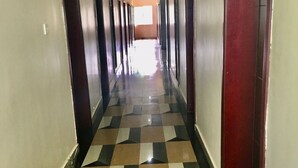 Un pasillo largo y estrecho con piso a cuadros, puertas a ambos lados y una fuente de luz al final.