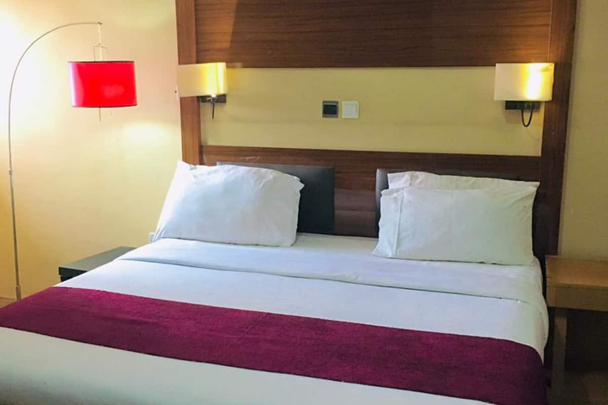 A hotel room with a large bed, two bedside lamps, and a red wall lamp.