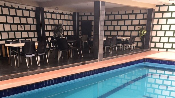 Una piscina con borde de azulejos, rodeada de una zona de estar con sillas y mesas.