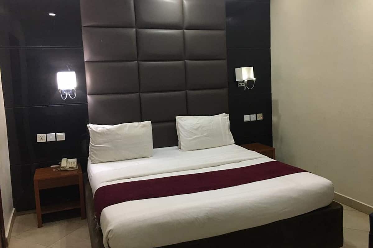 A modern hotel room with a large bed, two bedside tables, a phone on the left table, and wall-mounted lighting.