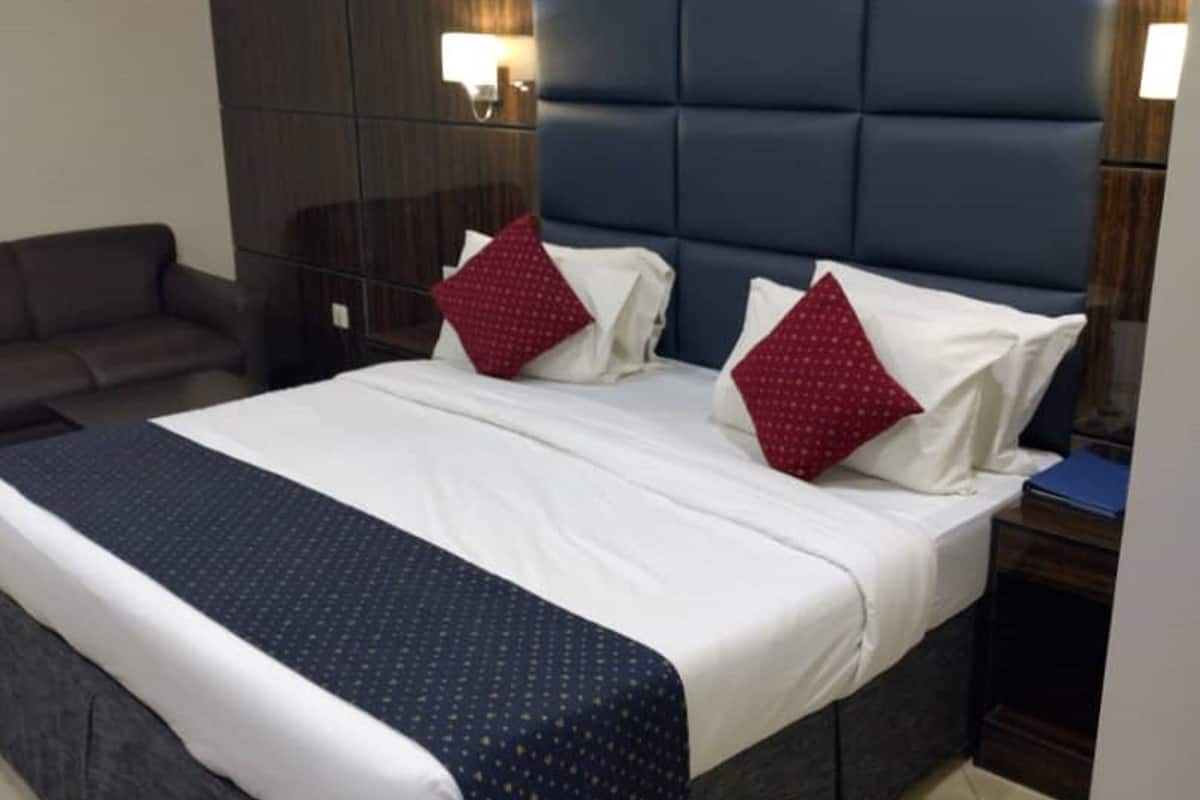 A hotel room with a large bed, a dark headboard, a nightstand, and a sofa.