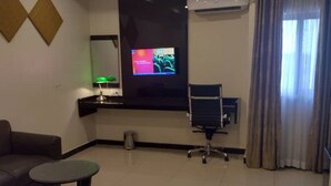 Una habitación de hotel con una cama, un sofá, una mesita, un televisor montado en la pared y una ventana con cortinas.