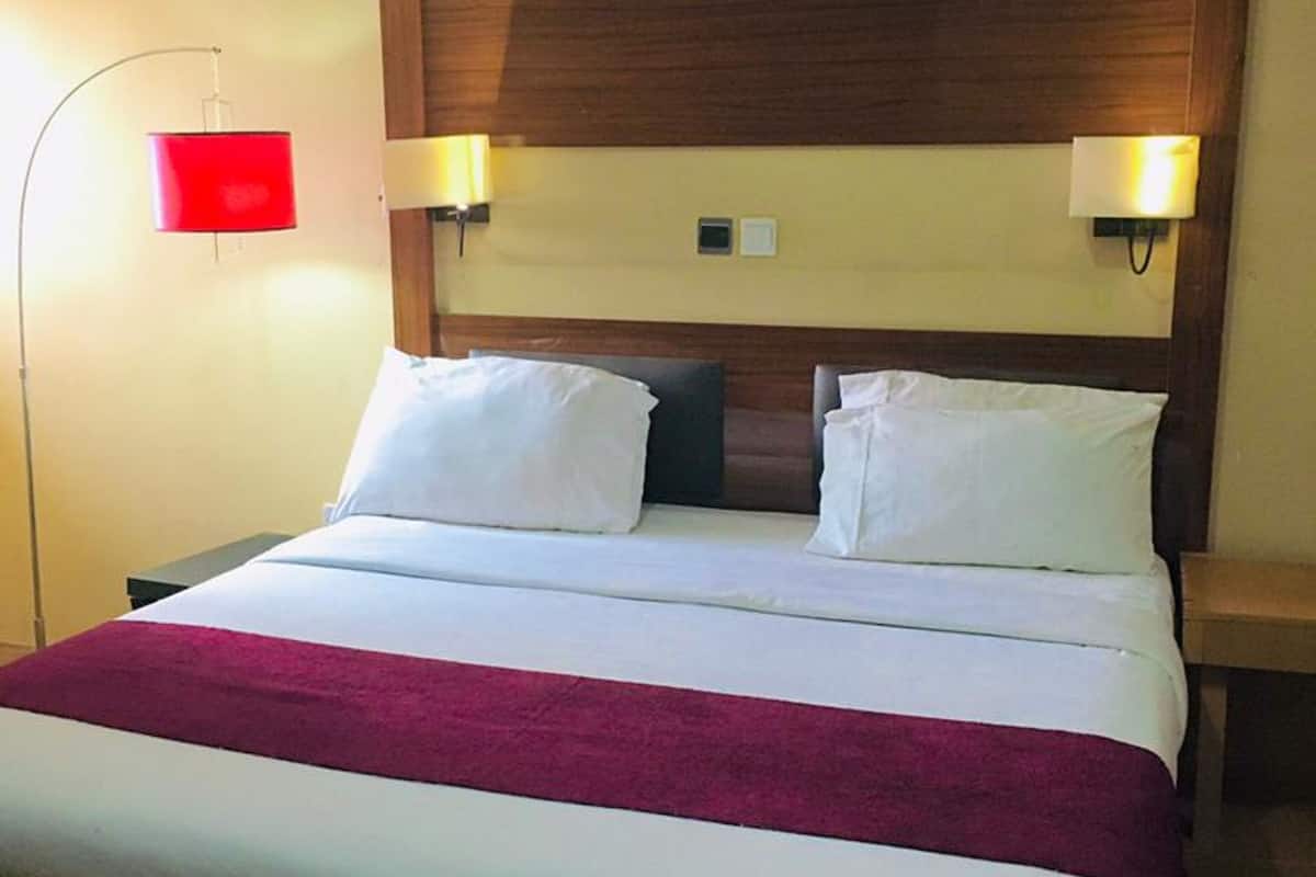 A hotel room with a bed, two bedside lamps, and a red wall lamp.
