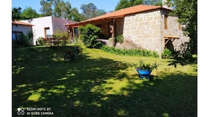 Una casa de piedra con techo de tejas, rodeada de un jardín cubierto de césped y árboles.