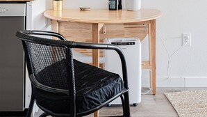 A kitchen with a wooden table, a black chair, a framed quote on the wall, and a small plant on the counter.